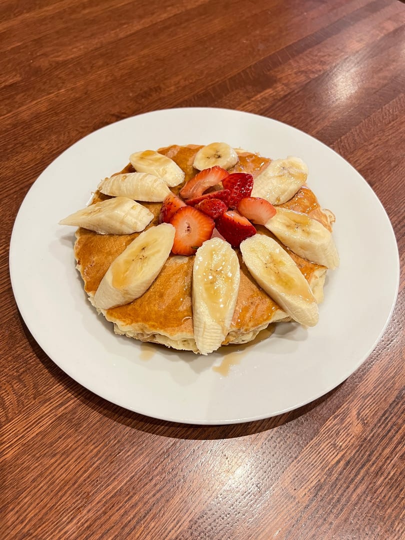 Fluffy pancakes topped with sliced bananas, strawberries, and a drizzle of syrup on a white plate.