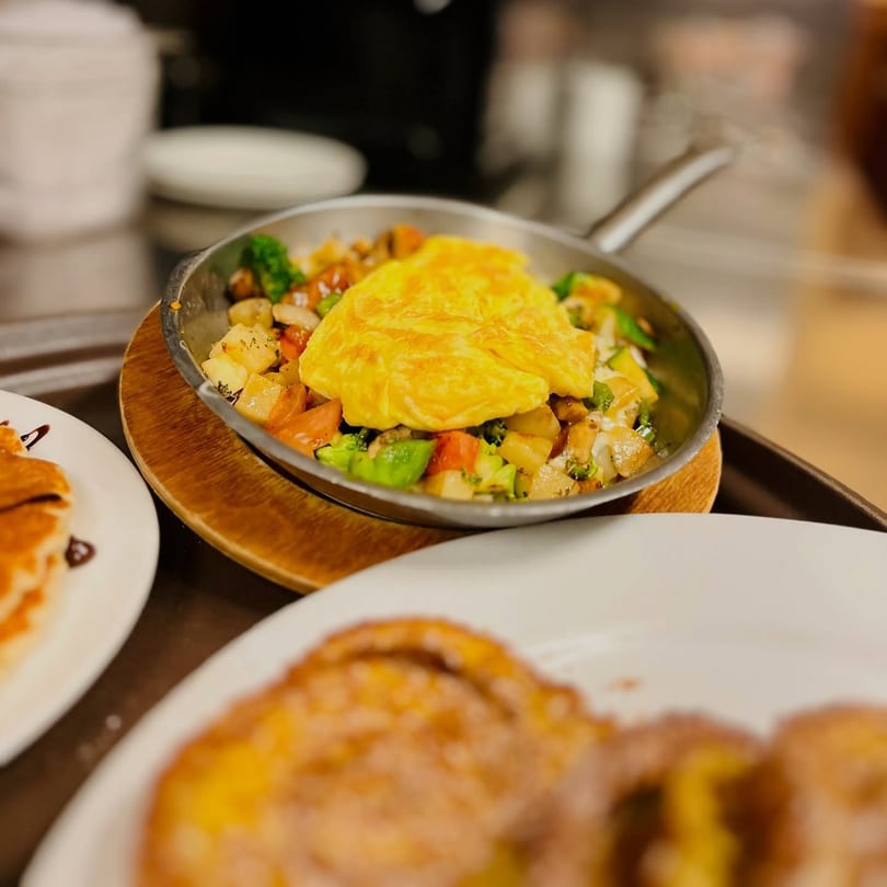 Omelet with diced vegetables and potatoes in a skillet, with pancakes and French toast nearby.